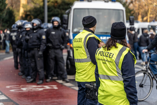 Communication Team of the german police is standing on the side of a demonstration. Safety vests are saying: "Police - Communication Team". Riot police in the background.