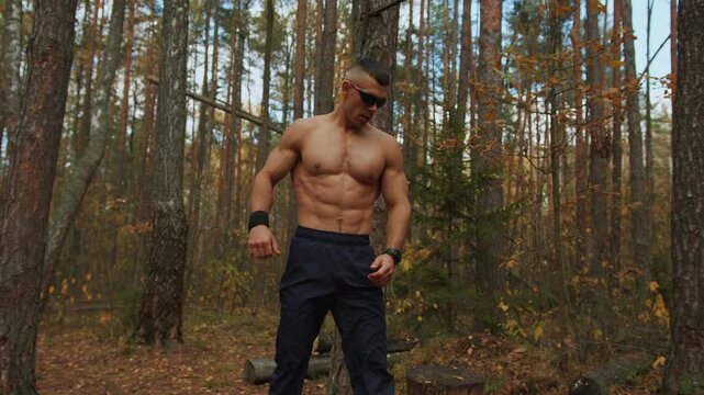 Young man in sunglasses restores breathing and shakes his arms after intense exercise on makeshift sports ground in an autumn forest. Sport and healthy lifestyle concept