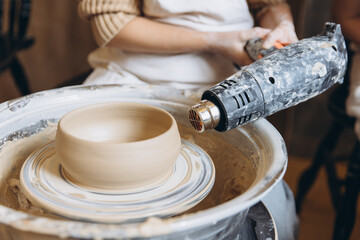 Person drying clay bowl on pottery wheel