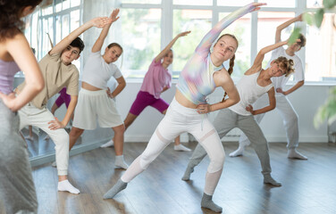 Obraz premium Group of boys and girls with teacher doing warm-up exercises before dancing in studio