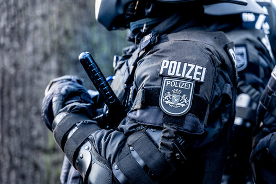 A german police officer is waiting in his riot body protection on a demonstration against the corona-laws. He has a tonfa or baton in his hand and a coat of arms of the city of Bremen on a badge.