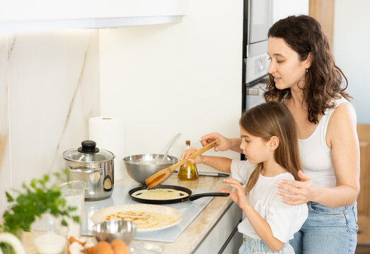 Happy mother and her preteen daughter frying pancakes on stove in the kitchen - Powered by Adobe