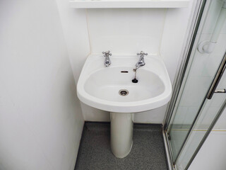 A white British style sink with two separate faucets and a drain. The sink is in a bathroom.