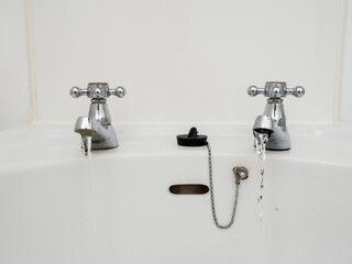 Two faucets are dripping water into a sink. The sink is dirty and the water is running