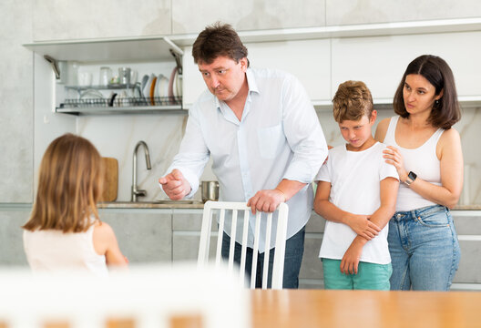 Mom and dad scold their guilty daughter standing in kitchen at home