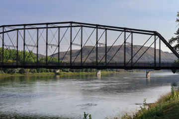 Fototapeta premium Close-up view of historic steel truss bridge over calm river with dry hills in background