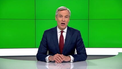 News anchor in studio. Journalist speaking. Man in suit and tie. News desk. Green screen background. TV presenter. News reporter. Formal wear. Professional setting. Broadcast studio. News program.