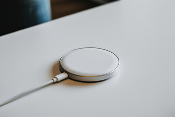 White circular wireless charger pad with an attached USB-C cable on a bright, smooth desktop, representing fast charging efficiency and contemporary design aesthetics.