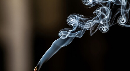 Smoke swirling from incense stick on dark background  