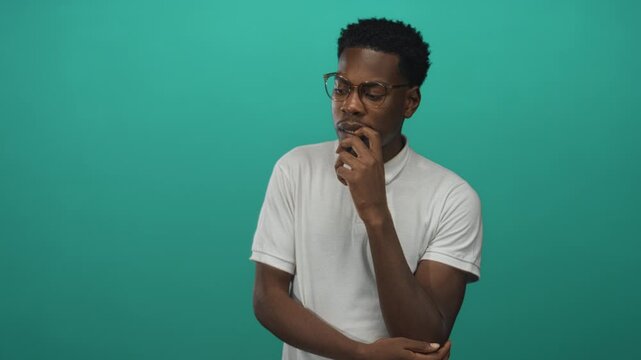 Man with finger on chin gesture in green studio, wearing eyeglasses and white polo shirt; contemplation.