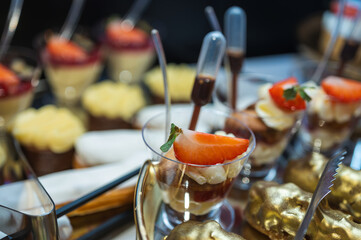 Close-up of beige vanilla macarons on a tray. Delicious French pastry dessert with cream and strawberry tarts in the blurred background. Sweet catering event concept, selective focus