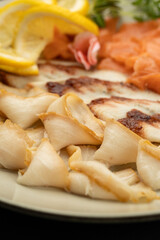 Close up of smoked fish slices with lemon garnish on plate, seafood appetizer macro