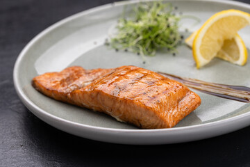 Grilled salmon fillet with lemon and microgreens on plate, gourmet restaurant plating