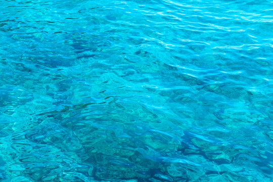 Crystal clear turquoise water surface with ripples and light reflections.