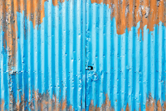 Corrugated metal wall with blue and orange peeling paint, rusty weathered industrial texture, abstract grunge pattern and metal door ring close up