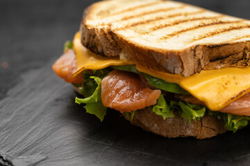 Grilled salmon and cheddar sandwich with lettuce on slate board, lemon and capers