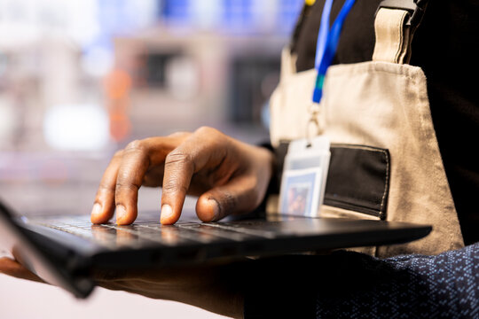 Industry 4.0 technician improves assembly line operations in industrial plant. Selective focus on African American engineer inputting digital optimization data on laptop to enhance automation systems.