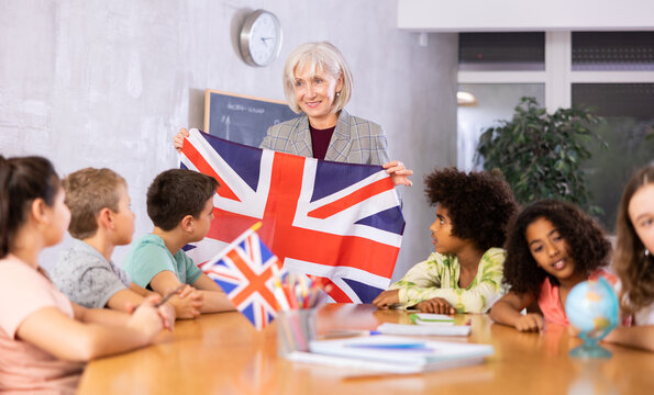 High school teacher holds the national flag of Great Britain in her hands and tells the pupils the history of the country - Powered by Adobe