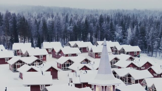 Drone footage showing a view of a village with a multitude of wooden cottages, with a snow-covered coniferous forest in the background. 4K.