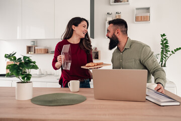 Happy couple enjoying breakfast and laughing in kitchen