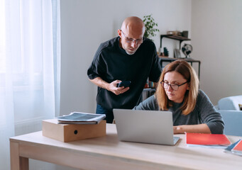 Small business owners focused on financial planning at home office, reviewing paperwork and managing online tasks on laptop, showing teamwork, responsibility and modern entrepreneurial workflow.