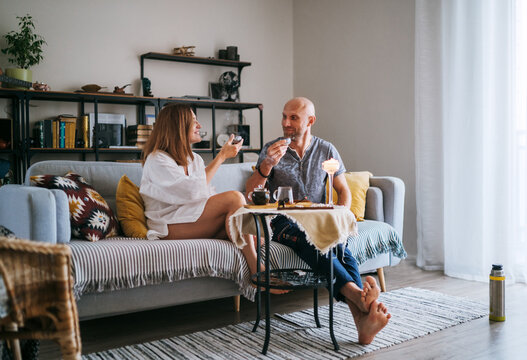 Relaxed couple drinking tea cozy living room sharing warm conversation, enjoying peaceful morning moment. Comforting home setting emphasizes connection mindfulness slow lifestyle intimate togetherness
