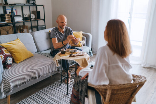 Relaxed couple drinking tea cozy living room sharing warm conversation, enjoying peaceful morning moment. Comforting home setting emphasizes connection mindfulness slow lifestyle intimate togetherness - Powered by Adobe