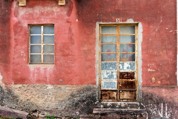 Vintage red wall with weathered frosted glass door and rusty window frame, textured abandoned house...
