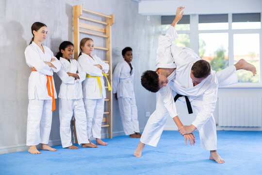 Adult man coach and boy in kimono practicing judo techniques in studio..