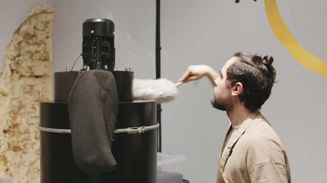An experienced barista uses a fluffy brush to keep the coffee roaster clean.
