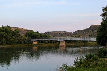 Bridge spanning river with hilly terrain and trees at sunset in panoramic landscape