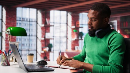 Smiling black man taking notes while watching a tutorial presentation, doing online self learning...