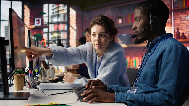 Call center manager doing training for worker providing live chat support, handling clients complaints. Team leader and intern dealing with unsatisfied customers, providing solutions, camera B