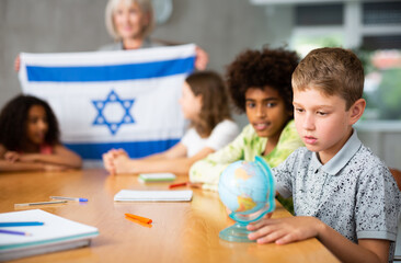 Fototapeta premium at entertaining geography lesson, children look at flag of Israel and listen to teacher s story about this country