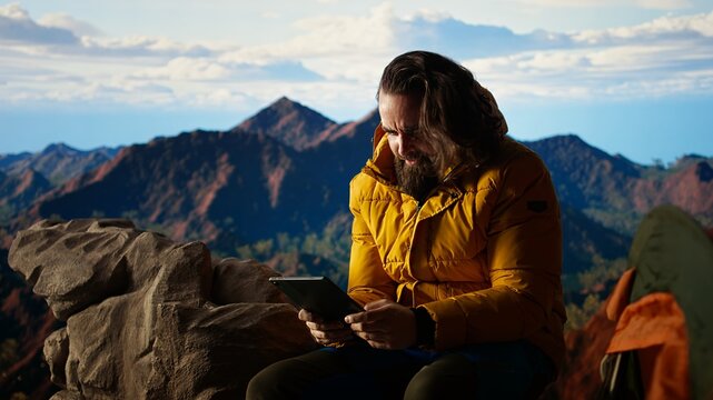 Male hiker struggles to work online in windy conditions on a remote mountain peak. Battling weak signals and cold weather, explorer is obsessed with technology and the internet. Camera A.