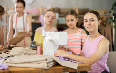 Child watches classmates work on creating clothes, school for young fashion designers and tailors. Optional classes for younger students, professional orientation, and familiarization with profession.