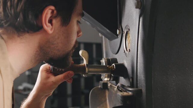A skilled barista focuses on the coffee roasting process in a cafe, checking the machine closely in the early morning light to achieve optimal flavor.