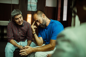 Adult men at therapy session, stressed and supportive in community room