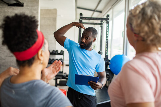 Adult male fitness trainer coaching women at gym, focused - Powered by Adobe