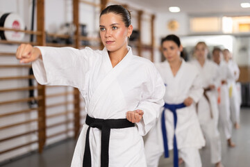 Assertive young woman practicing punches standing in row with others during karate classes © JackF