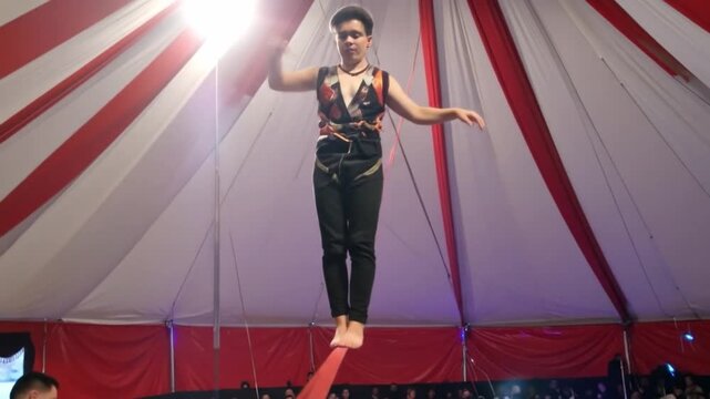 Aerial acrobat performing in a circus tent with red and white stripes