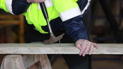 Closeup of male hands struggling to pry a nail from a wooden board with a hammer, tense awkward workshop moment