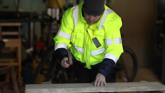 Man hammering a nail into a wooden board in a workshop, focused handwork with strong precise motion