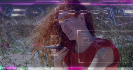 Speaking woman with red hair wearing sleeveless red top holding smartphone at dunes, with holograms