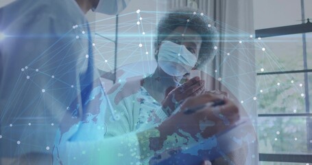 Sitting senior wearing surgical mask by paned window, nurse leaning in blue scrubs, network overlay