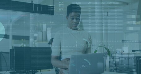 Standing worker wearing light top checking laptop and left monitor at office, HUD overlays