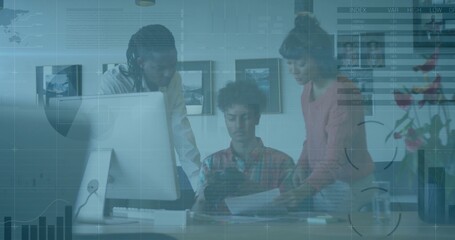 Reviewing 3 colleagues leaning at desk in office, wearing casual shirts with tablet and documents