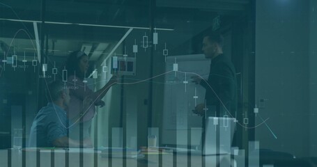 Presenting man in dark jacket pointing at flip chart in glass-walled room, laptop, market charts