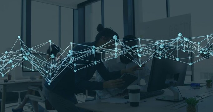 Collaborating team in jackets reviewing tablet and monitor in modern office with blue graph overlay