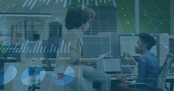 Discussing women examining charts in open-plan office in light blazer and dark shirt using tablet - Powered by Adobe